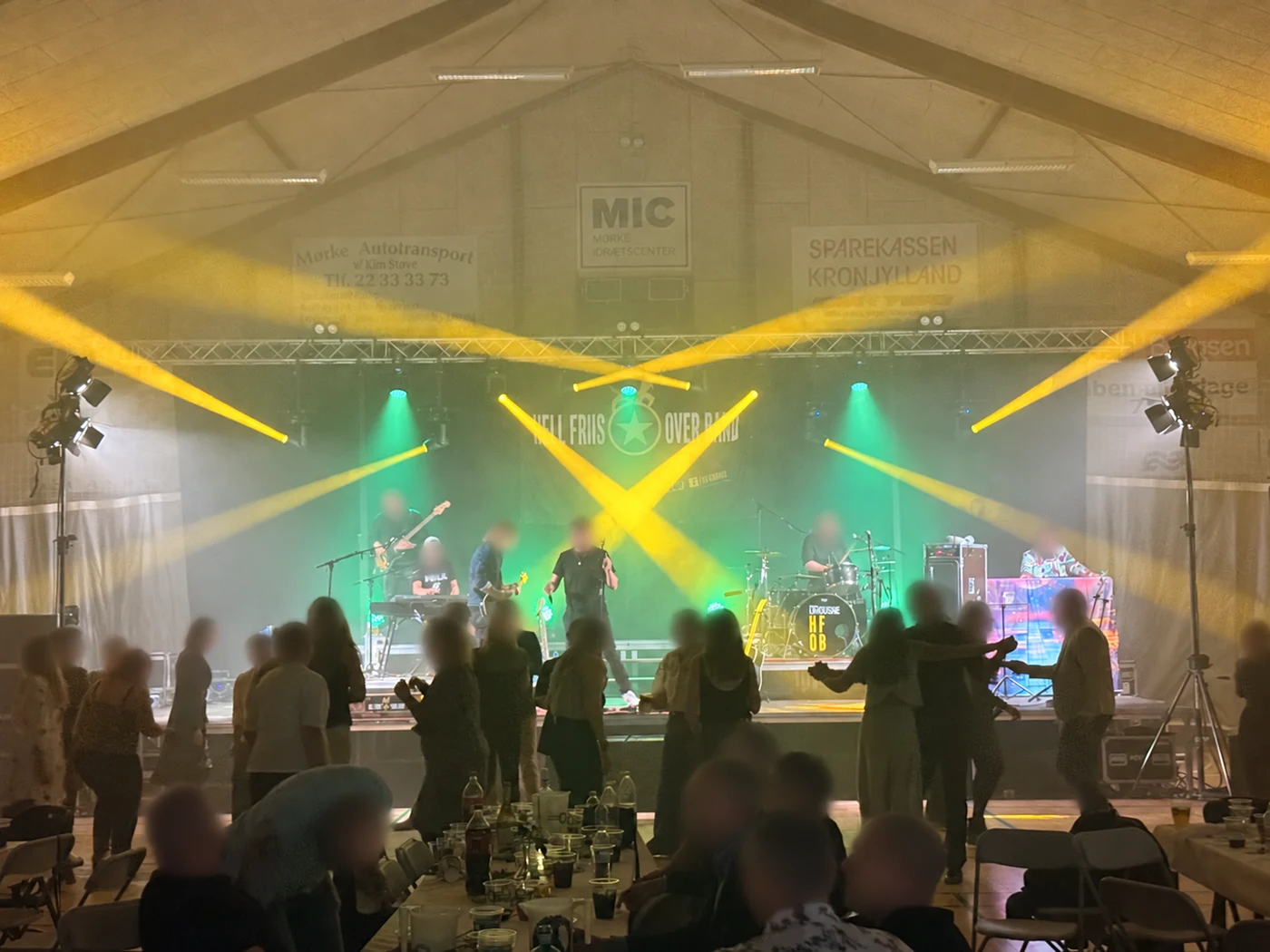 Yellow beams cross a green-lit stage while guests dance in front of a live band.