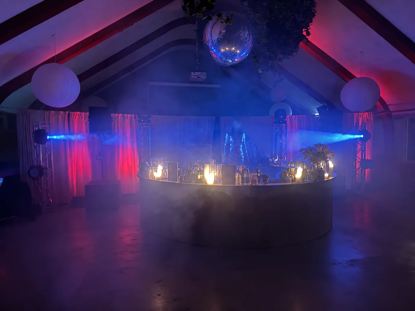 Blue beams and pink uplighting illuminate an event space with candles and a mirror ball.