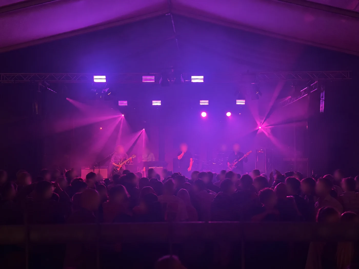 A live band performs for a crowd beneath purple and magenta stage lighting.